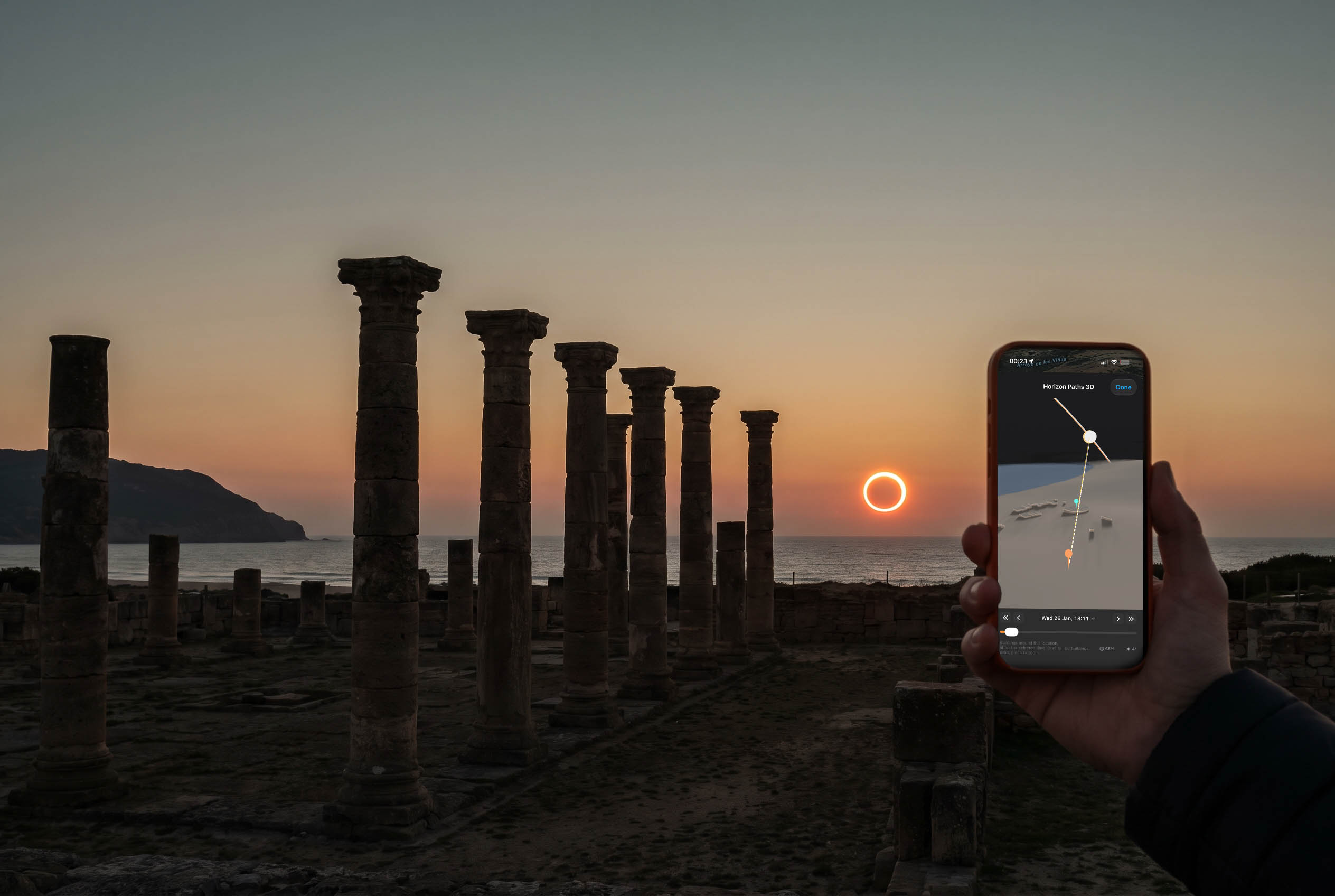 Visualisation of the 2028 ring of fire eclipse low over the Atlantic beside the Roman columns of Baelo Claudia, with a phone running Inverza held up in the foreground.