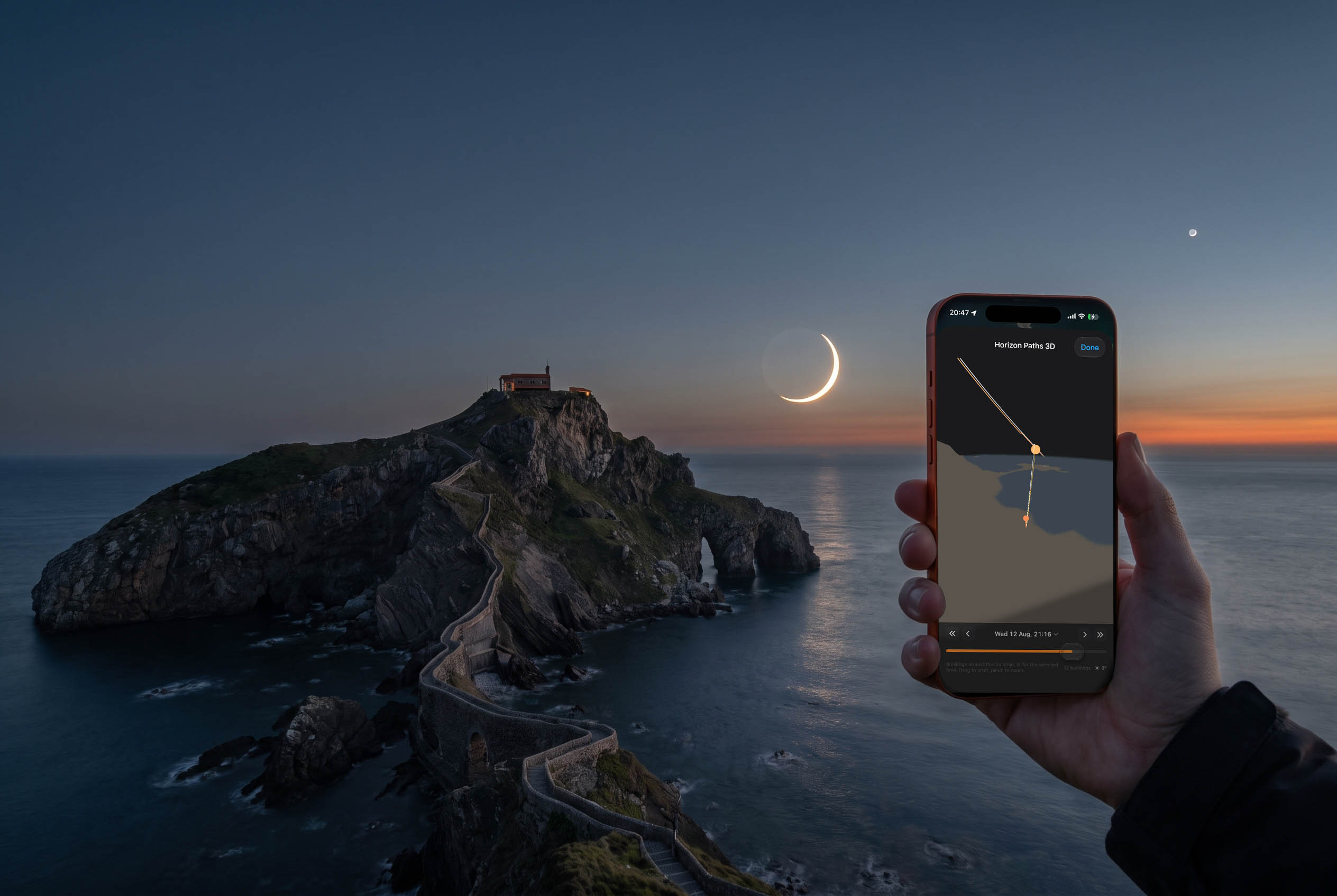 The 99.8% eclipsed sun as a razor-thin crescent low over the Atlantic beside the islet of San Juan de Gaztelugatxe, with a phone running Inverza held up in the foreground.